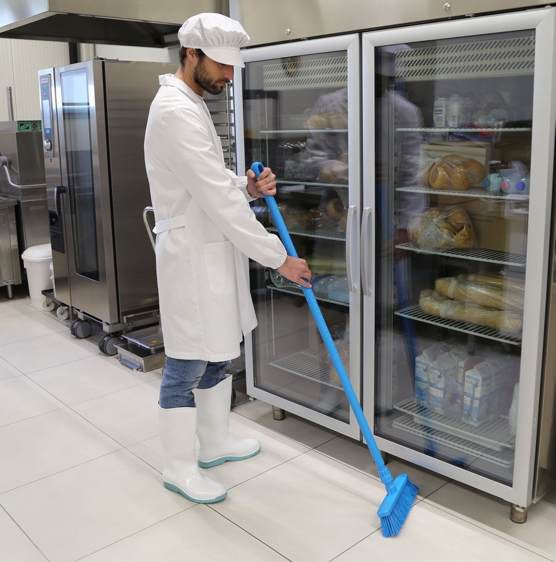 Pracownik zakładu spożywczego zamiata podłogę niebieską szczotką IGEAX z linii Hygiene